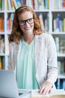 Portrait of smiling teacher using laptop in library