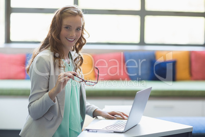 Portrait of smiling teacher using laptop in library