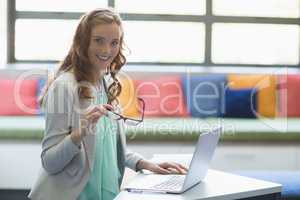 Portrait of smiling teacher using laptop in library