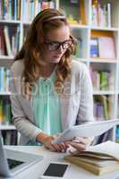 Teacher using digital tablet with laptop and phone on table in library