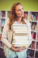 Thoughtful teacher holding a stack of books in library