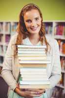 Portrait of smiling teacher holding a stack of books in library