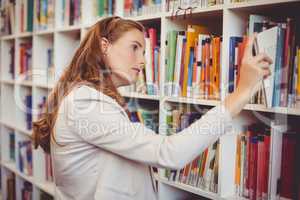 School teacher selecting a book from bookcase in library