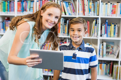 Portrait of teacher and school boy using digital tablet in library