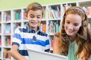Teacher and school boy using laptop in library
