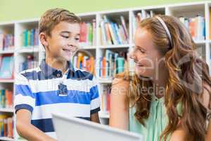 Teacher and school boy using laptop in library