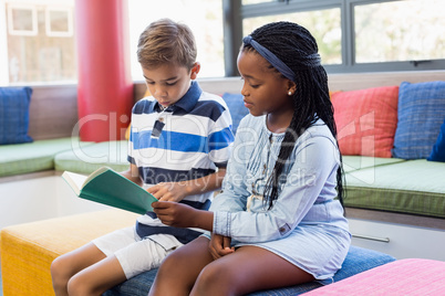 School kids sitting together on sofa and reading a book