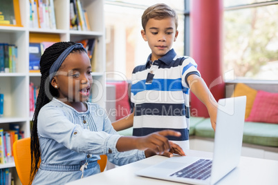 School kids using a laptop in library