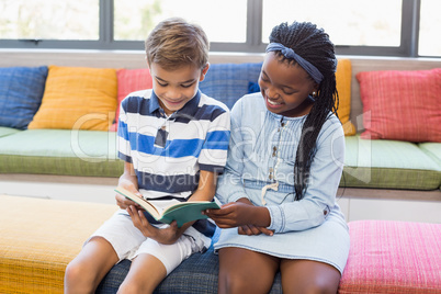 School kids sitting together on sofa and reading book