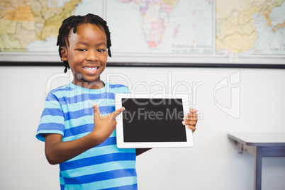 Portrait of schoolboy showing digital tablet in classroom