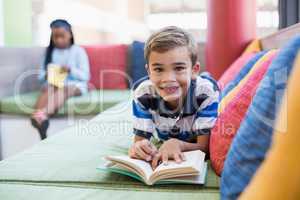 Schoolboy lying on sofa and reading book