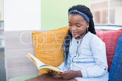 Schoolgirl sitting on sofa and reading book