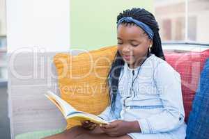 Schoolgirl sitting on sofa and reading book