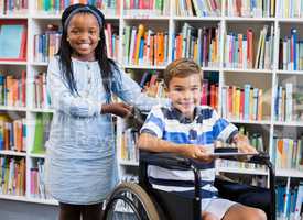 Happy schoolgirl standing with schoolboy on wheelchair