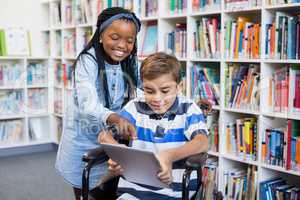 Happy schoolgirl standing with schoolboy on wheelchair using digital tablet