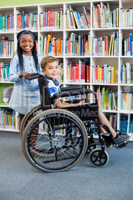 Happy schoolgirl standing with schoolboy on wheelchair