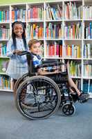 Happy schoolgirl standing with schoolboy on wheelchair