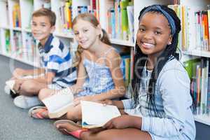 Portrait of school kids sitting on floor and reading book in library