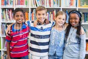 Smiling school kids standing with arm around in library