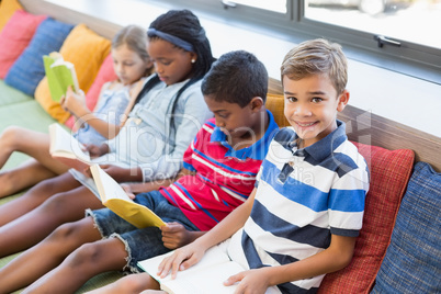 School kids sitting on sofa and reading book in library