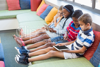 School kids sitting on sofa and using digital tablet in library