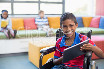 Disabled schoolboy on wheelchair using digital tablet in library