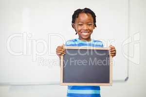 Portrait of smiling school boy holding slate in classroom