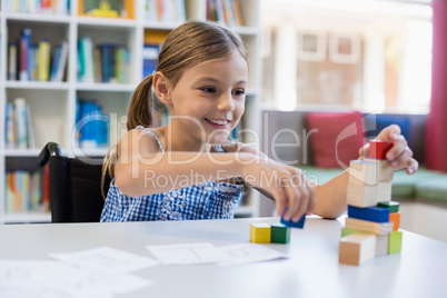 Smiling school girl playing with building block in library