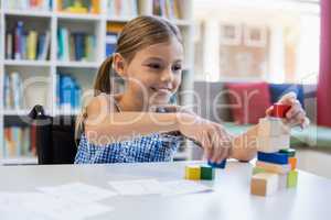 Smiling school girl playing with building block in library