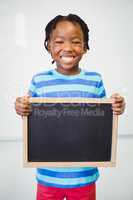 Portrait of smiling school boy holding slate in classroom