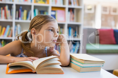 Thoughtful school girl reading book in library