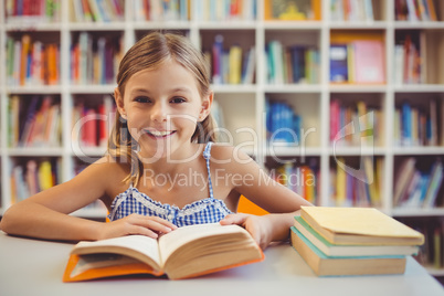 Smiling school girl reading a book in library