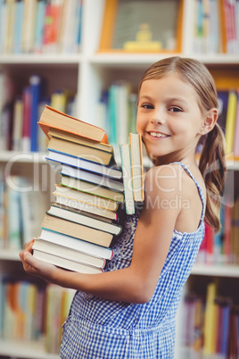 School girl holding stack of books in library