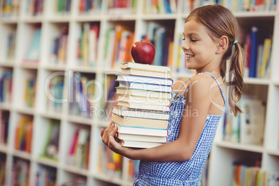 School girl holding stack of books in library