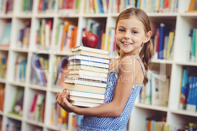 School girl holding stack of books in library