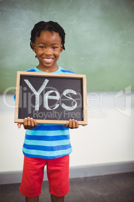 Schoolboy holding a slate in classroom which reads yes