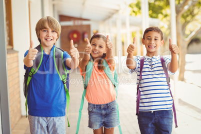 Smiling school kids showing thumbs up in school corridor