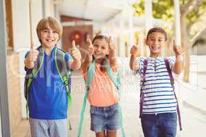 Smiling school kids showing thumbs up in school corridor
