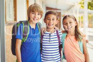 Smiling school kids standing in school corridor with arm around