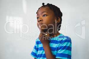 Thoughtful schoolboy standing with hand on chin in classroom