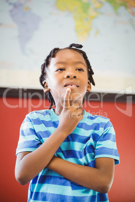 Thoughtful schoolboy standing with hand on chin in classroom