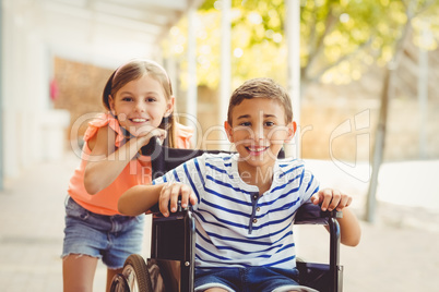 Happy schoolgirl standing with schoolboy on wheelchair