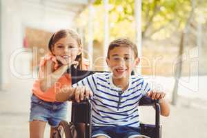 Happy schoolgirl standing with schoolboy on wheelchair