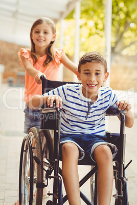 Happy schoolgirl pushing a boy on wheelchair