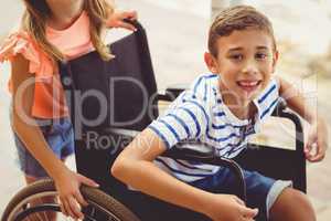 Happy schoolgirl pushing a boy on wheelchair