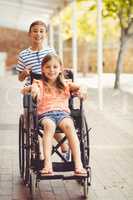 Happy schoolboy pushing a girl on wheelchair