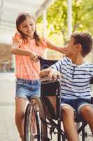 Happy schoolgirl pushing a boy on wheelchair