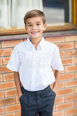 Happy schoolboy standing in corridor with hands in pocket