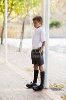 Thoughtful schoolboy leaning on pole with hands in pocket