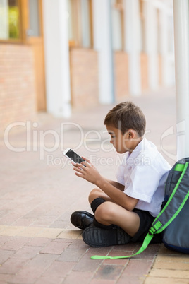 Schoolboy sitting in corridor and using digital tablet